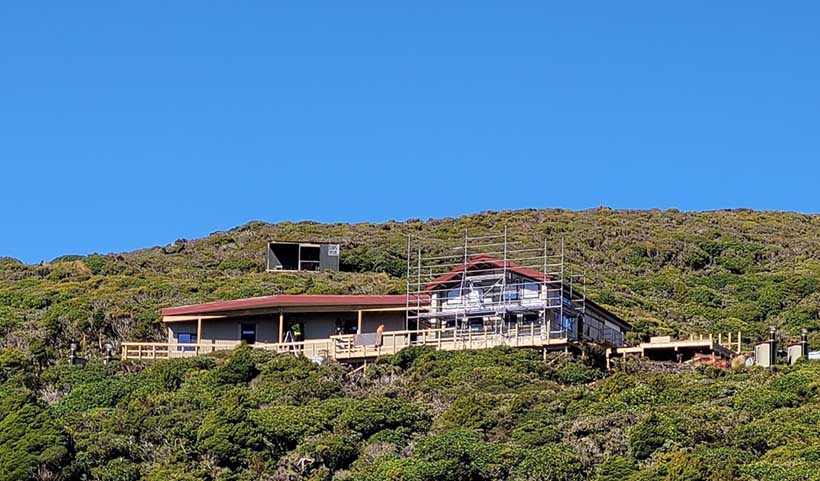 View of hut in the middle distance with workers and scaffolding in place.