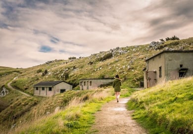 Woman walking among disused buildings on hill slope.