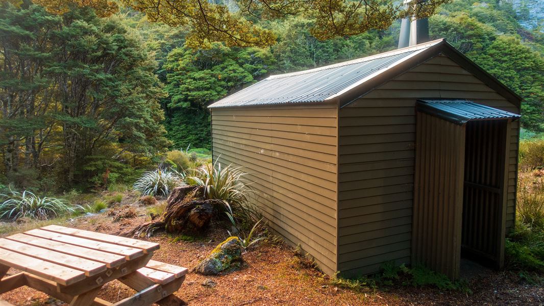 Small building by picnic table and trees.