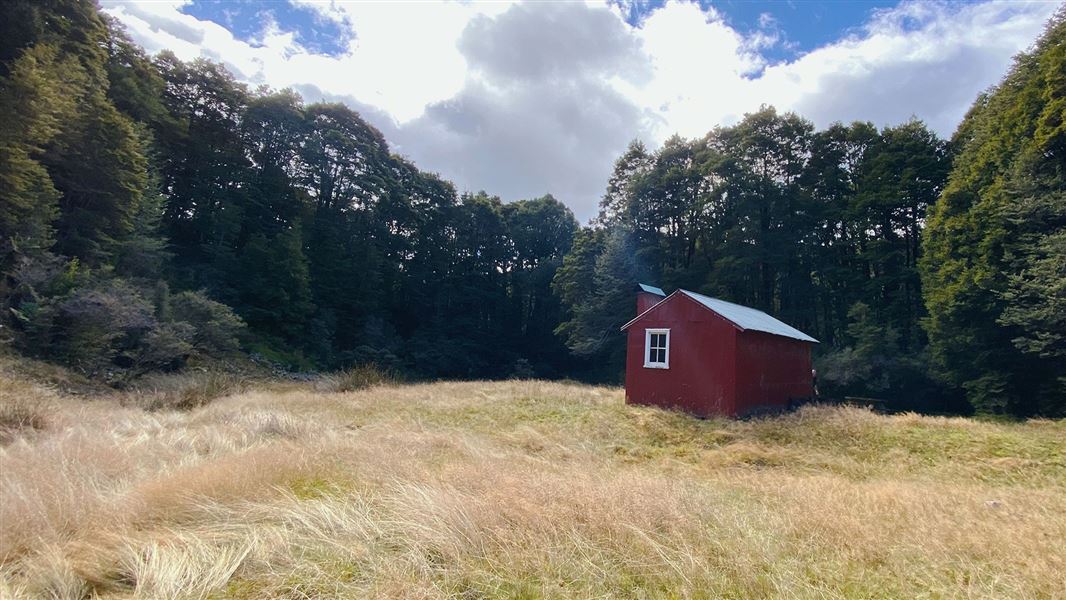 Small single story building in grass by trees.