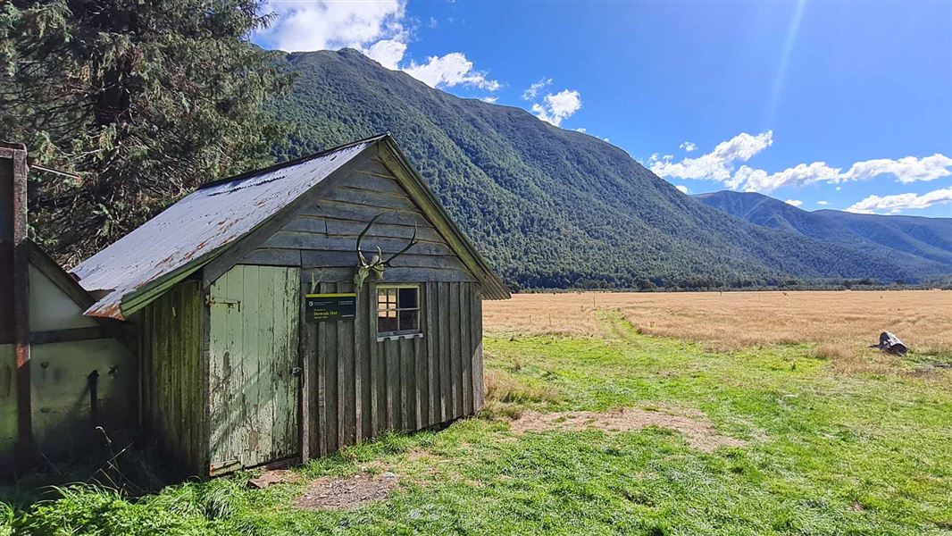 Old hut on a grassy plain with bush covered ranges in the distance. 