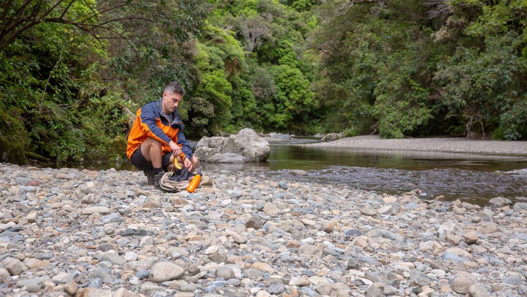 A man by a river packing a banana skin away. 