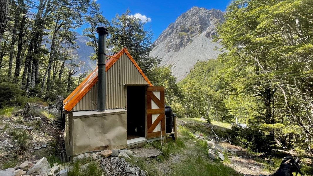 Tin hut with chimney and mountain peak behind. 