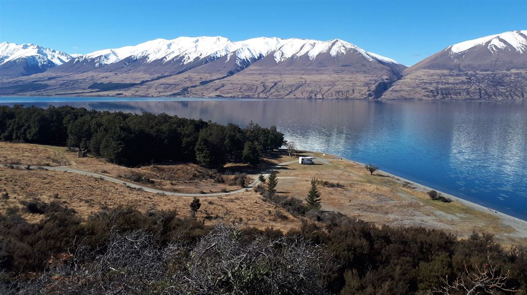 Motorhome next to lake with mountains in background. 