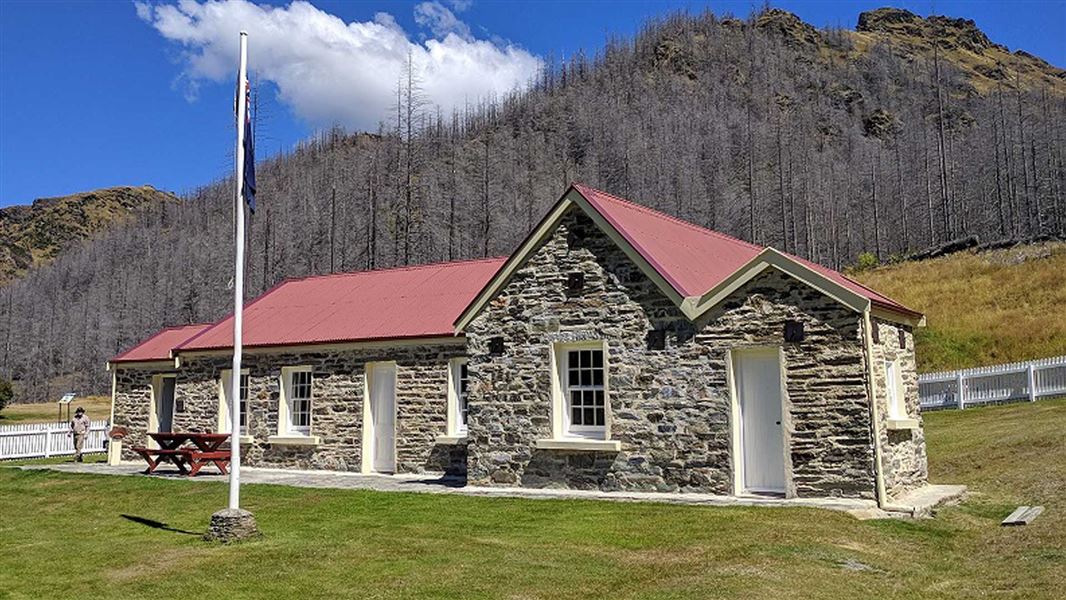 Historic stone building with a pitched red roof and flag pole.