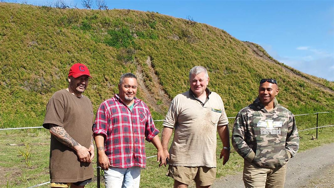 Four men standing in front of shrubland