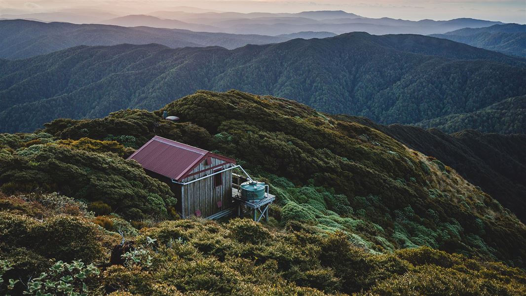 View of bush covered hills with small wooden building.