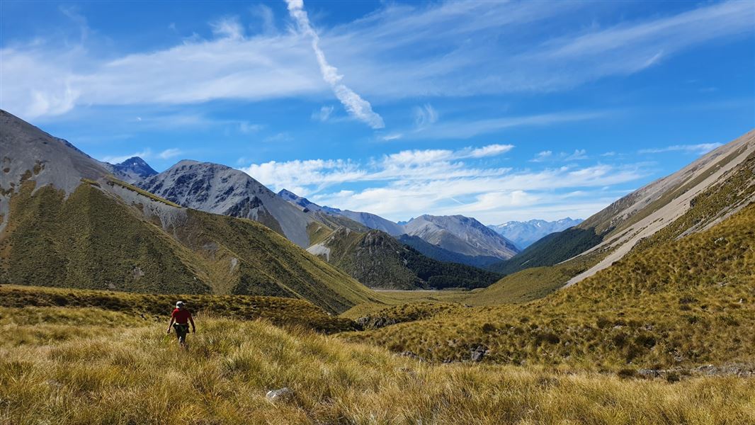 Grassy valley with blue sky and person walking