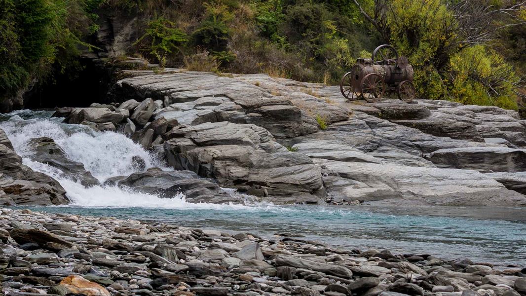 River running down rocks with rusted old steam engine on the rocks.