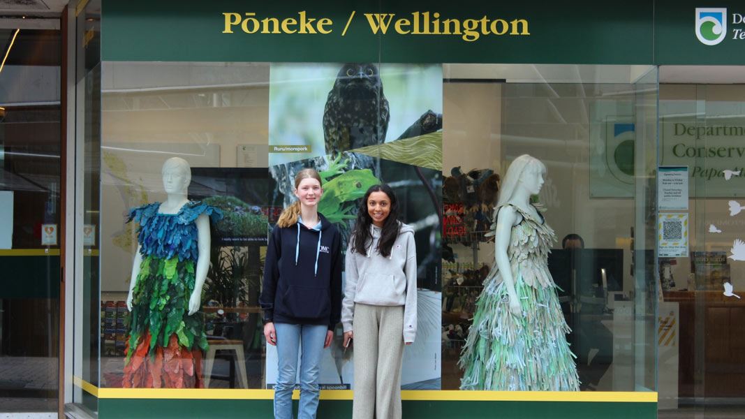 Students outside visitor centre window displaying their dresses. 