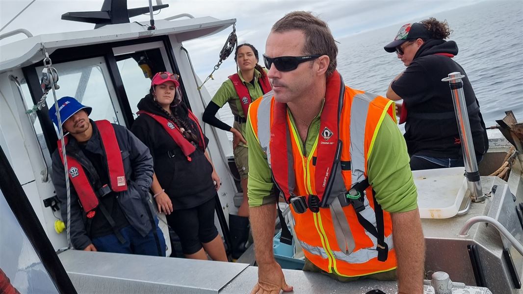 A picture of DOC ranger Stew Robertson looking out from a boat in open water, with several iwi members also on board.