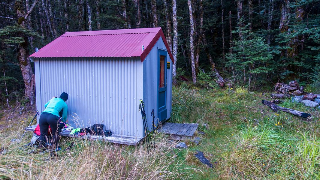 Small building by trees with person in front.