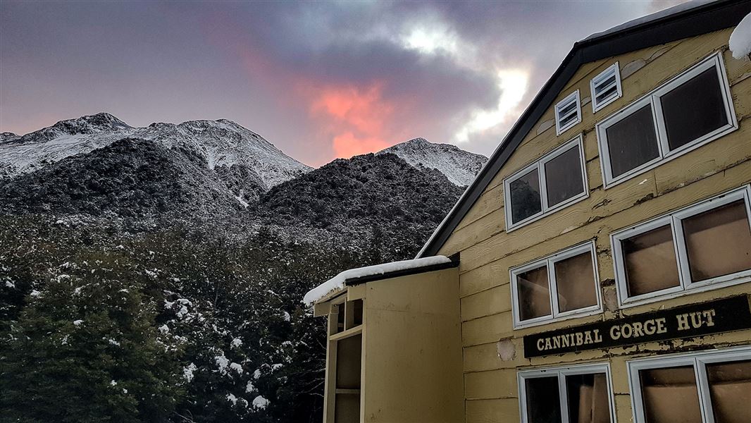 Wooden building in front of snowy hill.