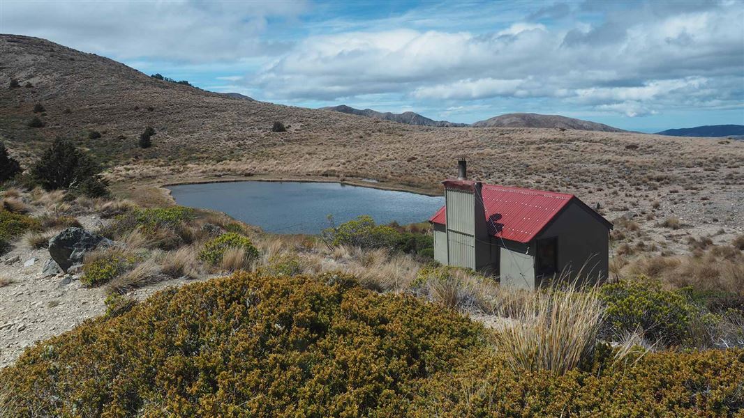 Hut on grassy plain with small tarn in background. 