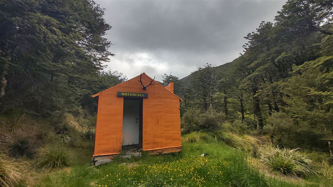 Small orange building on grass by trees.