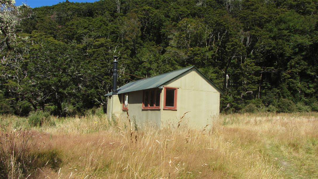 Small building in dry grass by hill.