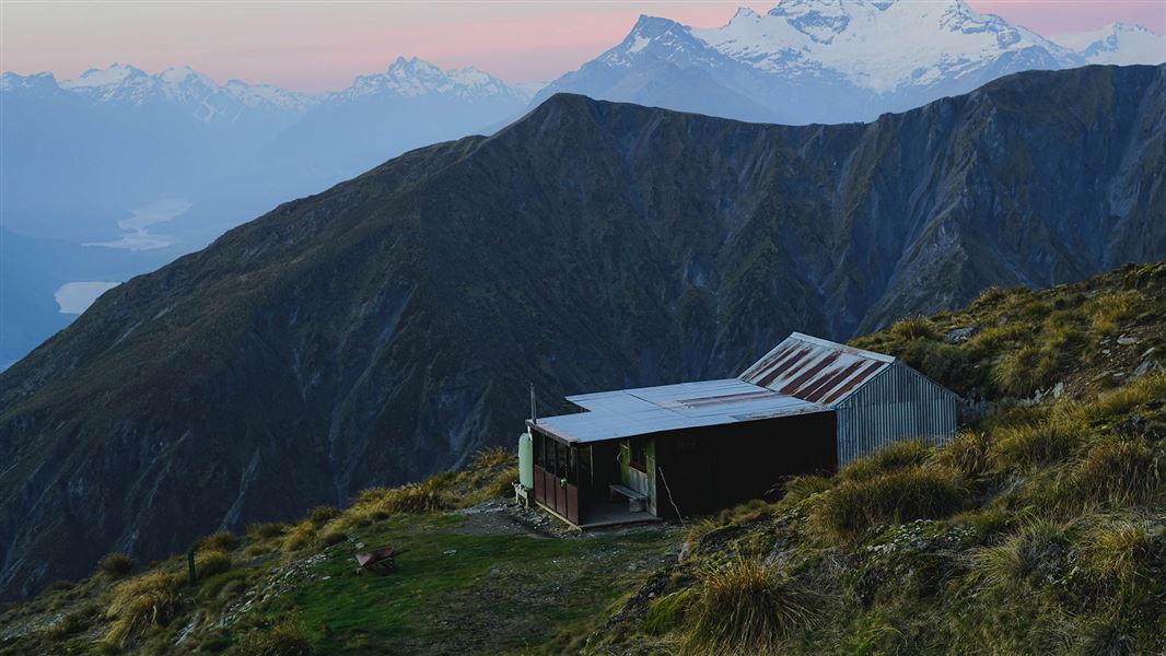 Small building on grass with view of mountains.