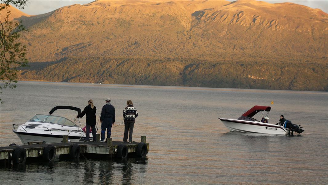 Two boats on lake at dusk, people standing on one boat.