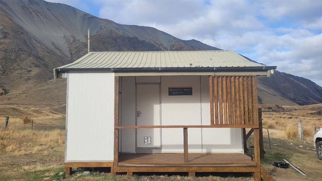 A white freshly painted hut in front of a mountainous landscape.