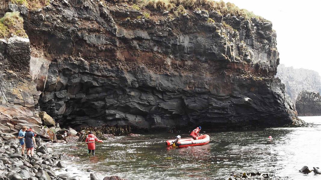 People on a small boat land in a small alcove.