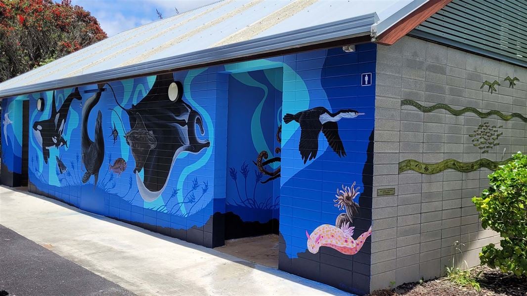 The wall of a toilet block covered by paintings of marine species including orca, seals, and birds.