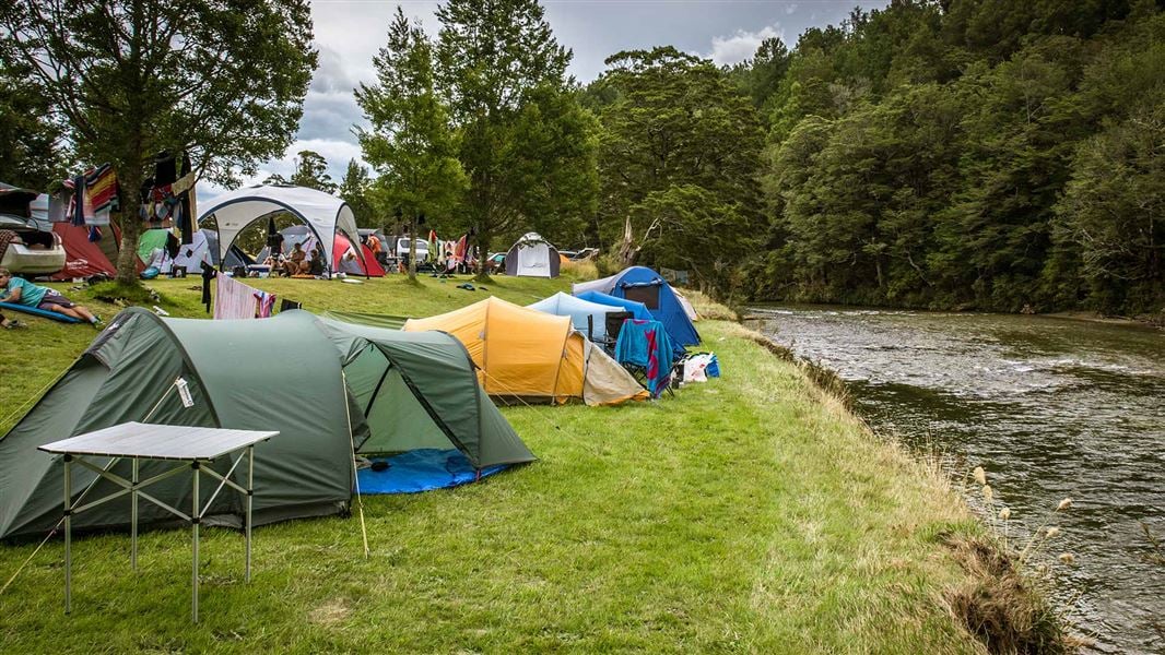 Tents on a grassy flat by a river.