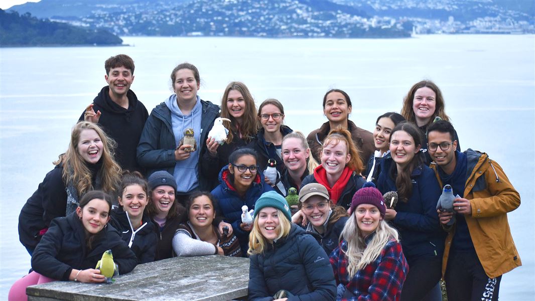 Young people grouped around a picnic table with the Wellington harbour and hills behind them.