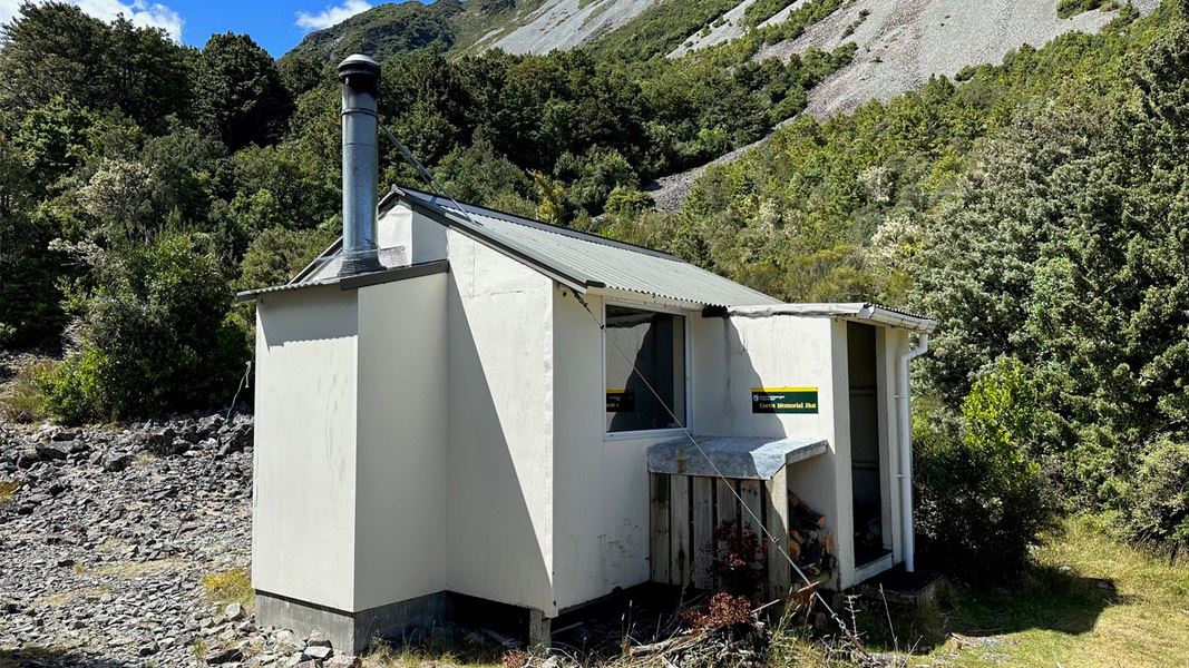 Small hut with chimney in front of high ridge behind. 