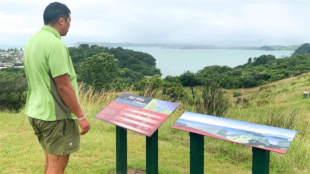 A DOC ranger seen from behind looking at the two new panels at the top of the hill.