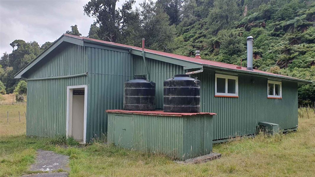 A green coloured single storey building in a clearing next to a forest.