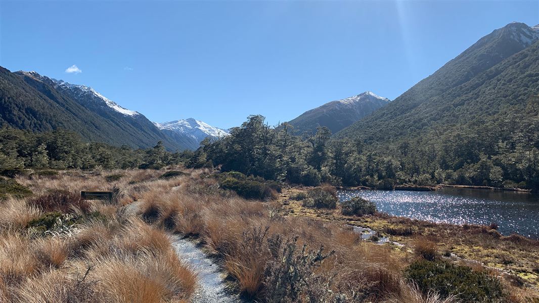 Walking track by river with snowy mountains in background. 