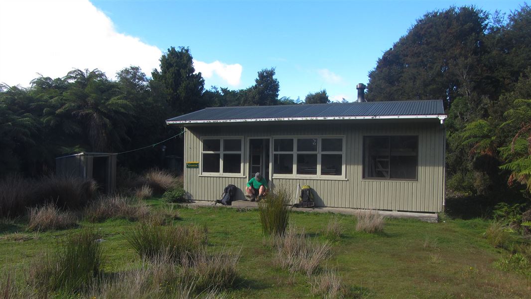 Small building near trees with person sitting on doorstep.