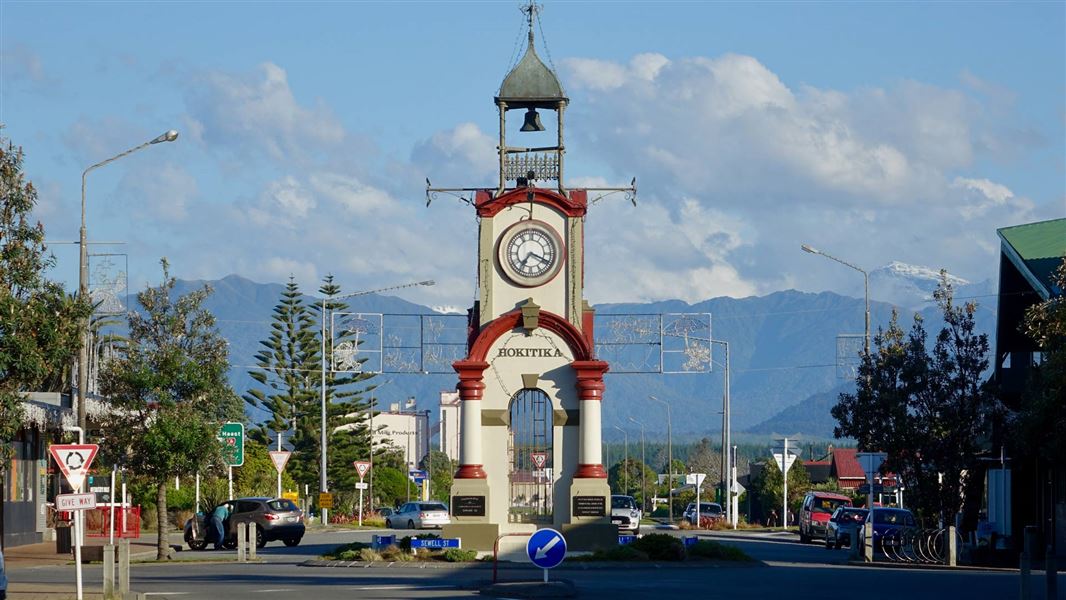 Heritage clock tower in the centre of a road round about with hillside behind.