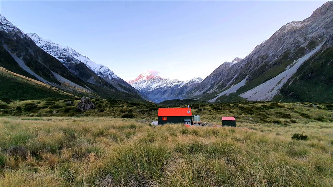 Small building by snowy mountains.