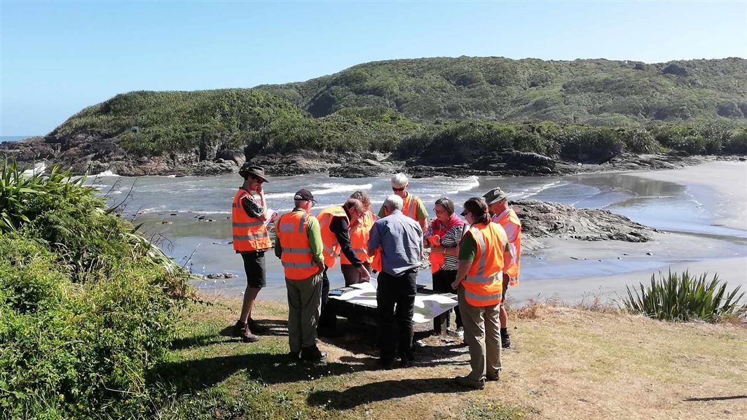 A group of people in high-vis look at a map on a beach.