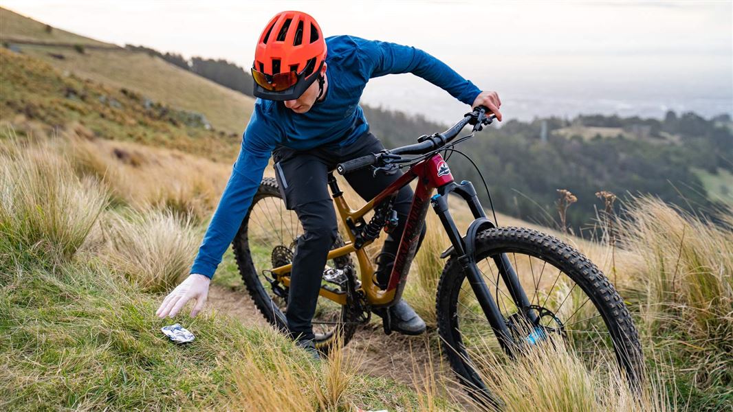 A cyclist stopping to pick up litter on a hill track.