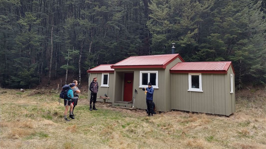 Hut on grassy flat by trees.