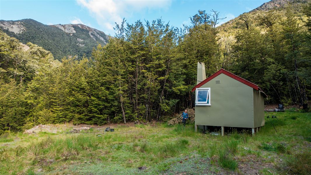 Small building by trees with hills in distance.