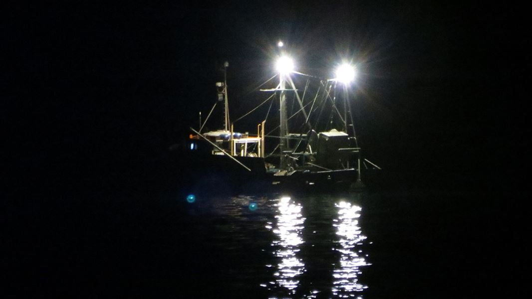 A fishing boat at sea, photographed at night, with two bright white lights on the mast.