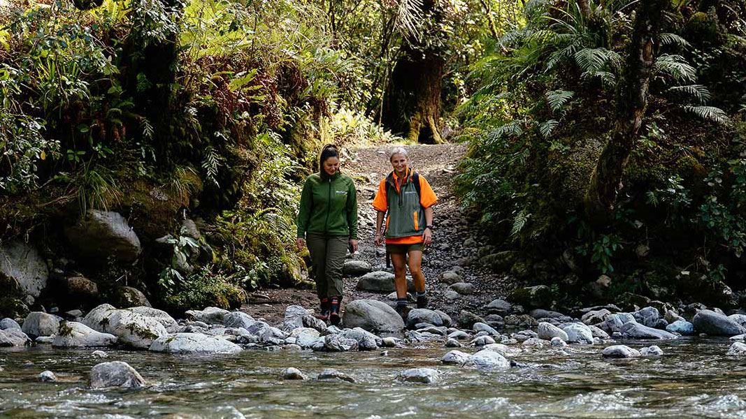 Two rangers walking on a trail towards a river.