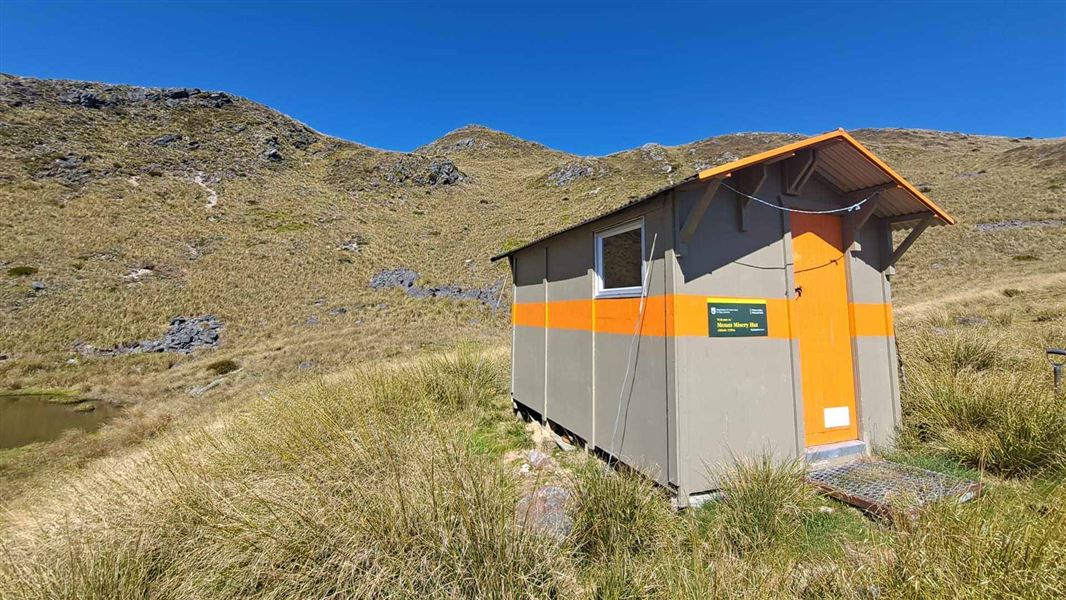 Hut on ridge top surrounded with tussock .