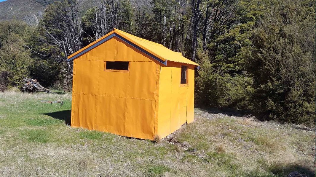 An orange small cabin in a small clearing in the forest.