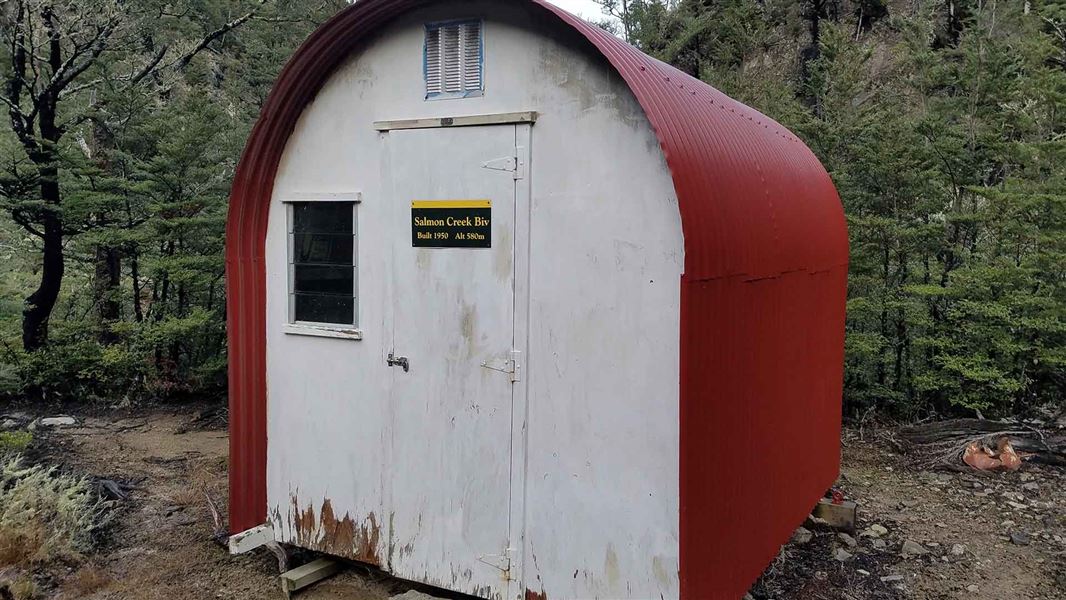 A small white and red metal cabin in the woods.