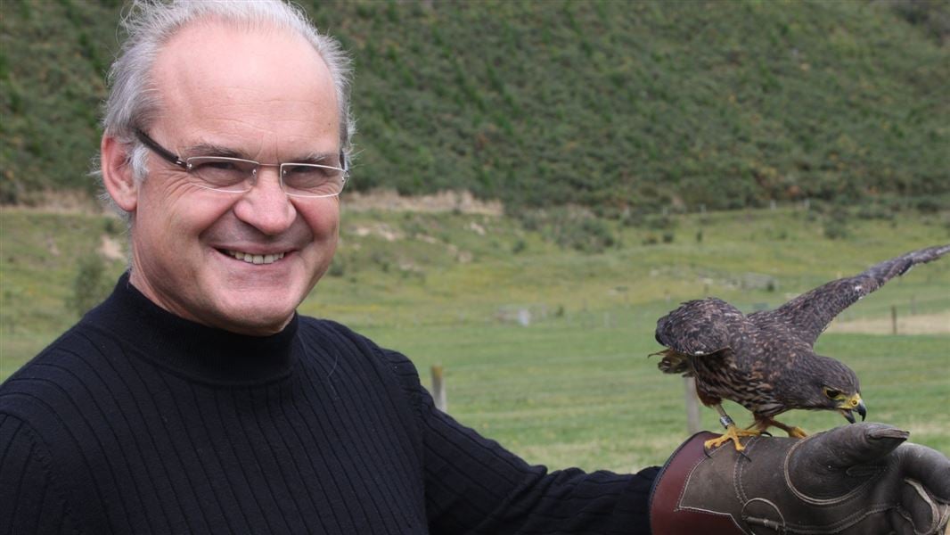 A man smiling with a NZ Falcon perched on his right hand's glove.