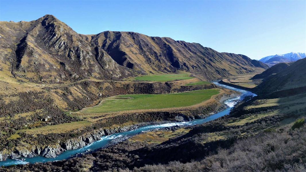 River following through mountain range with snow capped range in the distance..