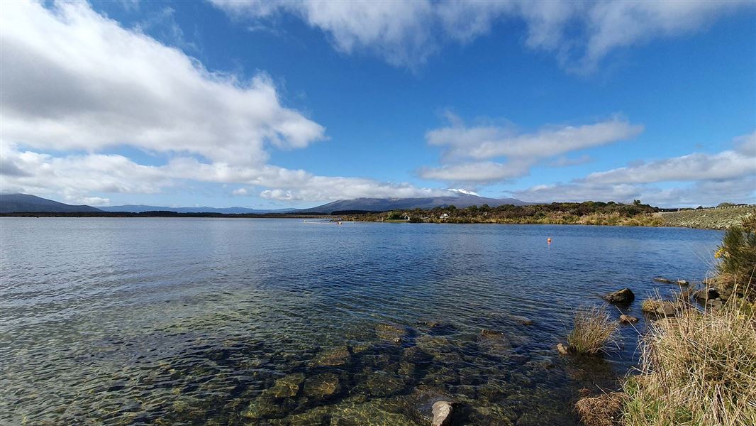 A clear lake on a sunny day with a mountain in the distance.