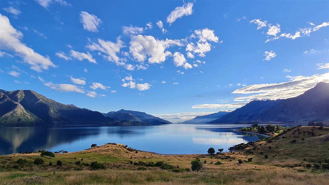 Landscape with lake in centre with sky reflection and steep green peaks behind. 