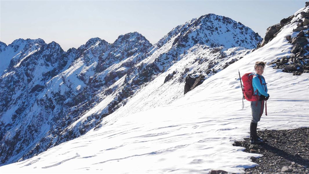 Tramper on top of snow capped ridge with Mt Rolleston in the background. 