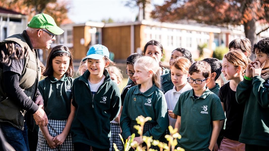 A teacher talks to a group of primary school students outside.