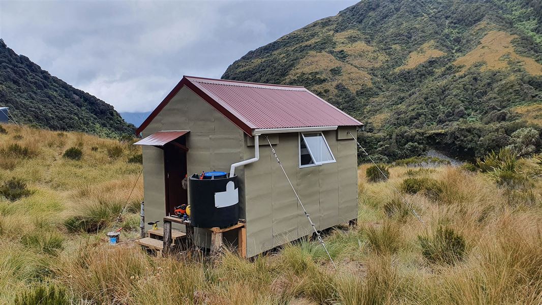 Small building on grass by hills.